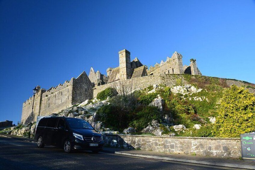 A historic stone castle on a hill, a black car parked in front, and a clear blue sky. 3