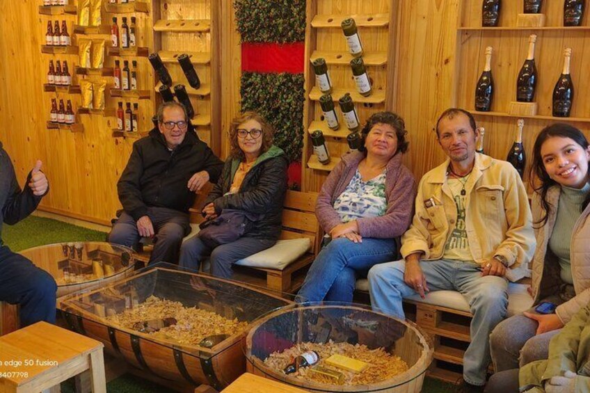 A group of people seated in a room with wooden walls and shelves of wine bottles. 3