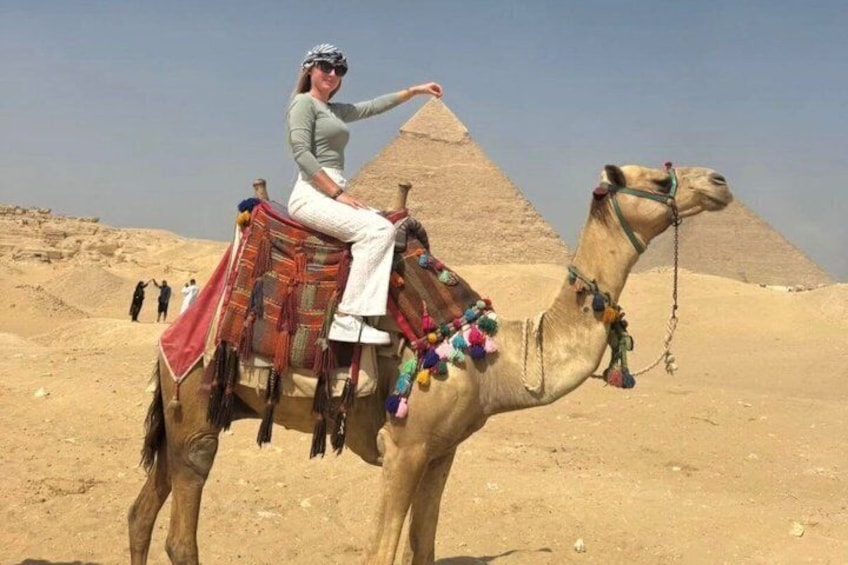 A person riding a camel with a decorated saddle in front of the Great Pyramid of Giza. 1