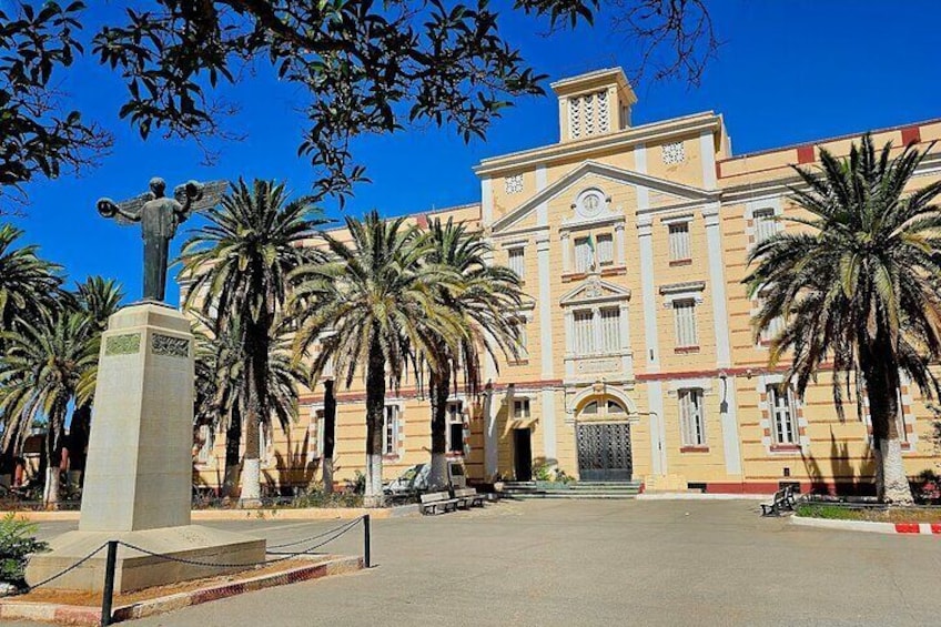 A historic building with palm trees in front, a statue, and a clear blue sky. 4