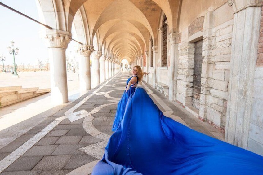 A person in a blue dress sitting on a bench in a covered walkway with arches and stone walls. 1