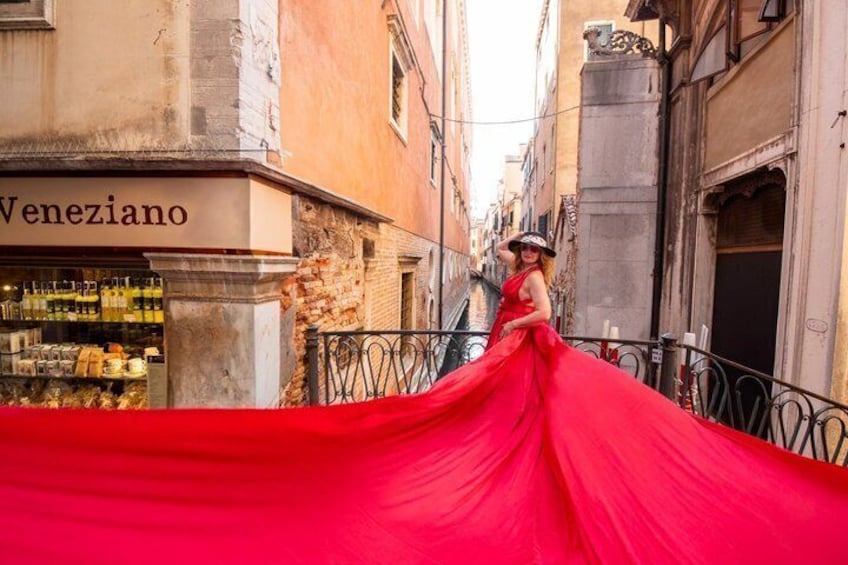 A person in a red dress standing on a balcony with a view of a street and a building labeled 'Veneziano.' 5