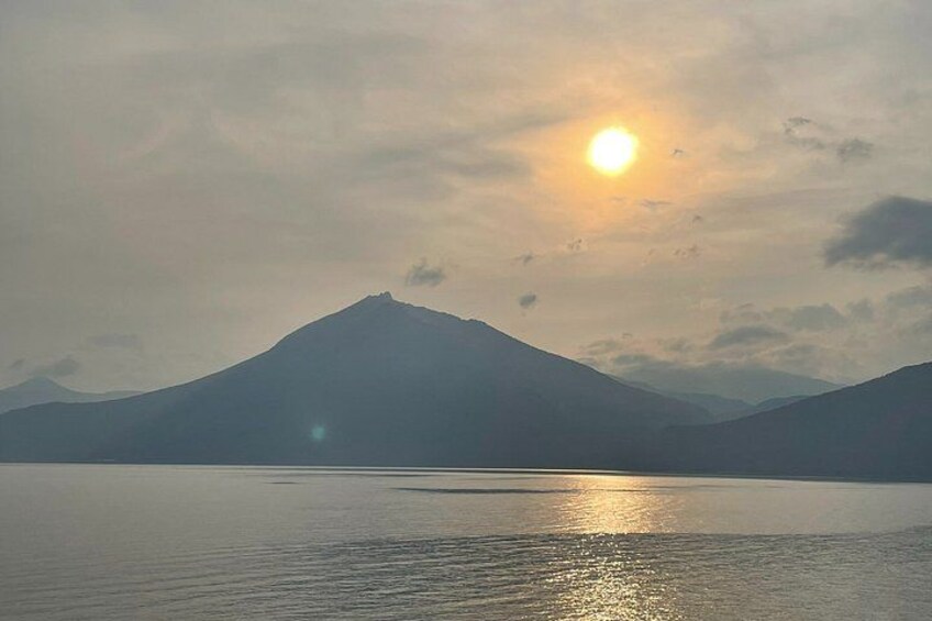 A mountain range, a body of water, and a sun setting or rising in the sky. 1