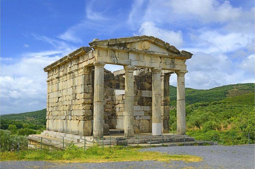 An ancient stone structure with columns, surrounded by greenery and hills. 4