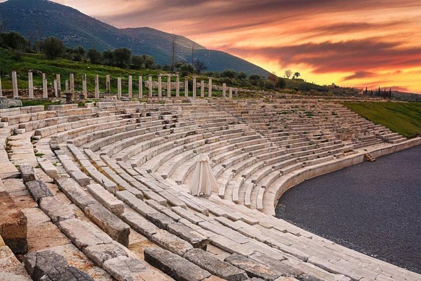 An ancient amphitheater with stone seating and a stage, surrounded by a hilly landscape. 1