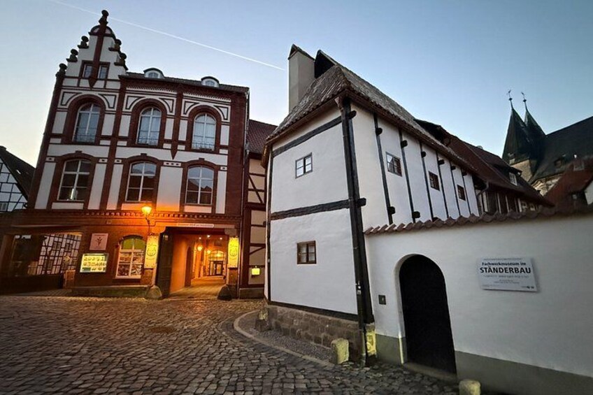 A cobblestone street with traditional European architecture, including a building with a sign reading 'Standerbau.' 4