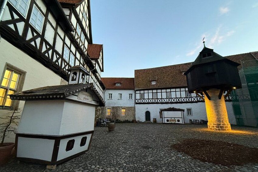 A courtyard with cobblestone ground, traditional half-timbered buildings, and a small tower structure. 5