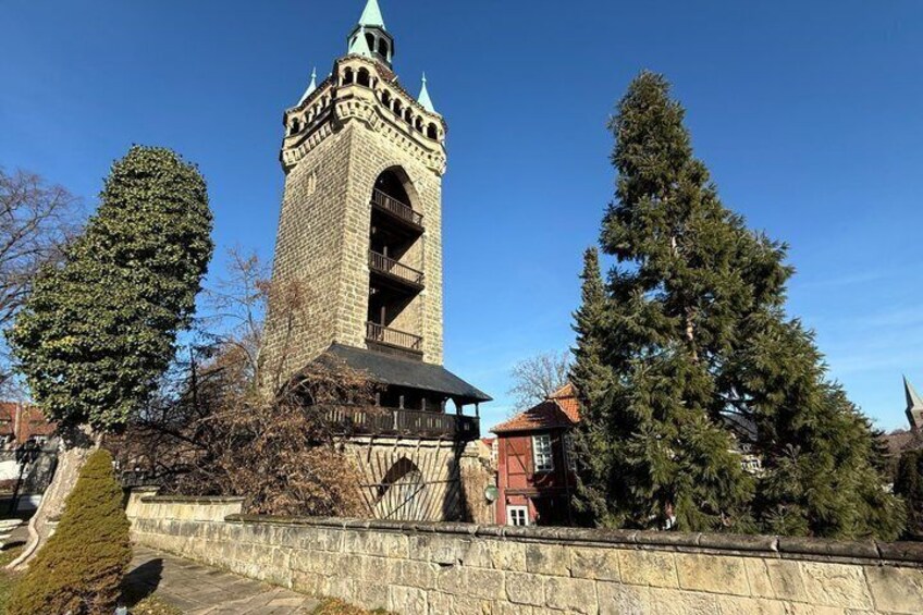 A historic tower with a clock, surrounded by trees and a stone wall. 5