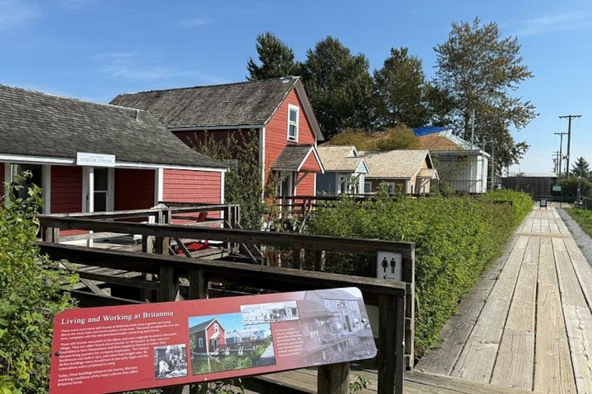 A wooden boardwalk leading to red buildings with a signboard about living and working at Britannia. 2
