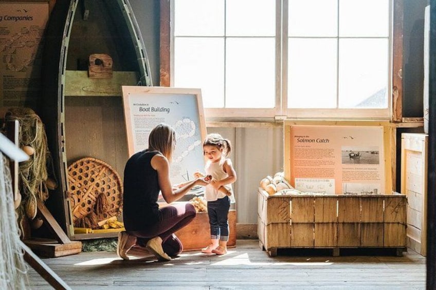 A woman and a child in a boat-building exhibit, wooden crates, and informational posters. 3
