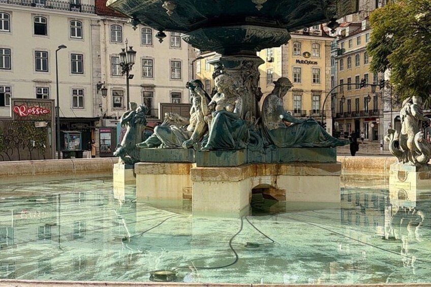 A fountain with statues, surrounded by buildings and a clear sky. 3