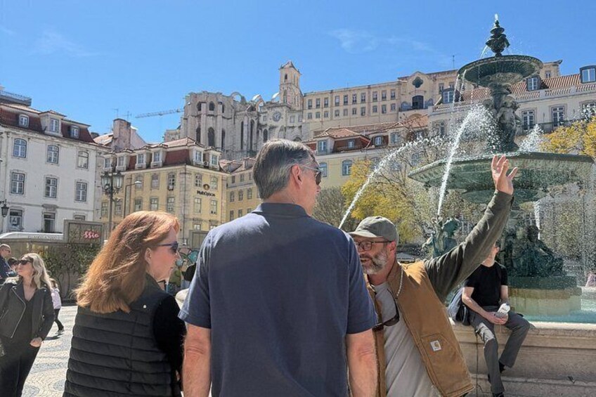 A group of people near a fountain with a historic building in the background. 5