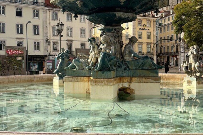 A classical fountain with statues, surrounded by buildings and a clear water surface. 3