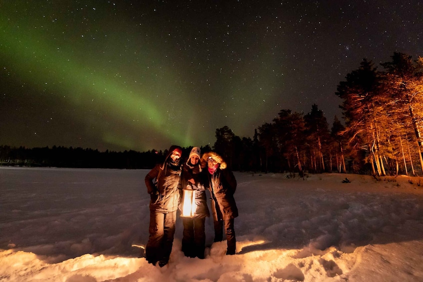 Three people standing in the snow under a starry night sky with the aurora borealis. 3