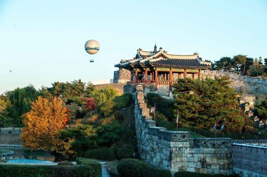 A traditional Korean palace with a stone wall, a hot air balloon, and autumn foliage. 3