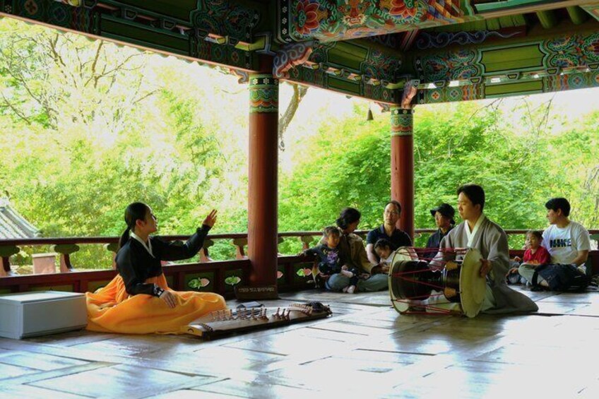 A traditional Korean gathering with people seated on the floor, a drum, and a person playing the drum. 1