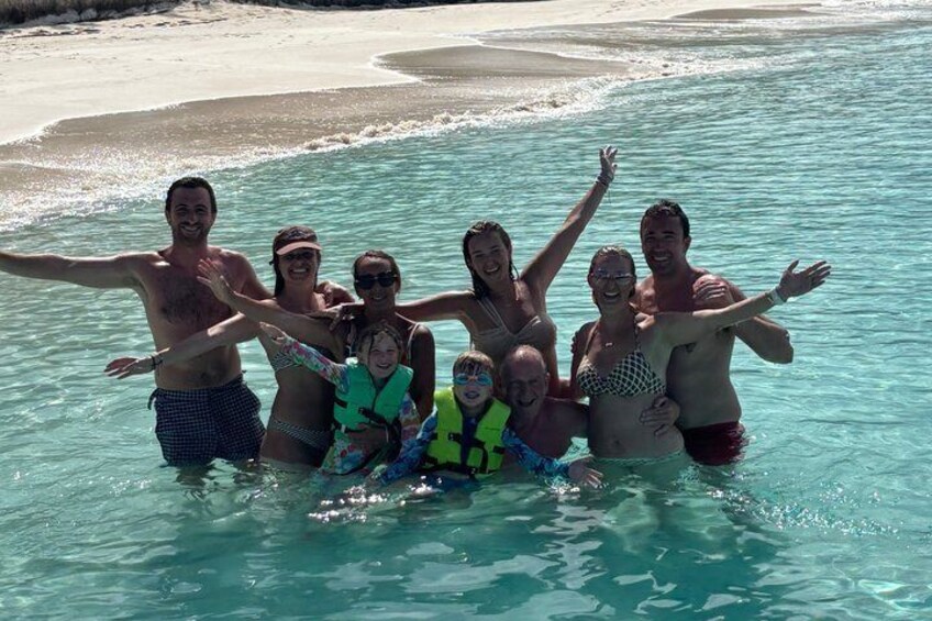 A group of people in a shallow, clear body of water with a sandy beach in the background. 1
