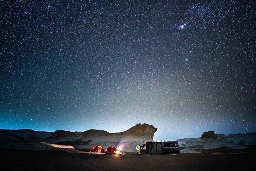 A starry night sky over a desert landscape with a vehicle and tents. 4