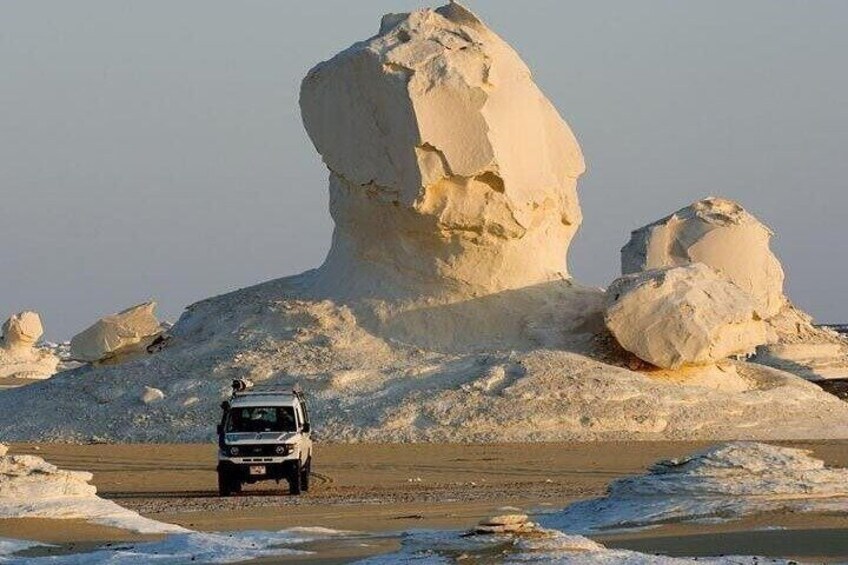 A vehicle on a sandy terrain with large rock formations in the background. 3