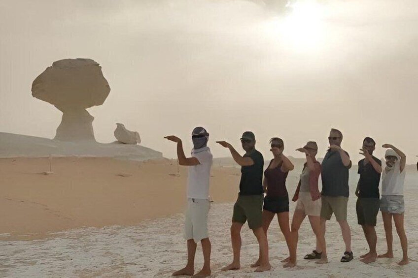 A group of people standing on a beach with a large rock formation in the background. 5
