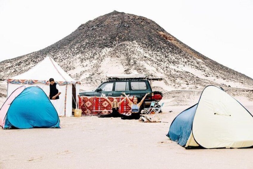 A desert campsite with tents, a vehicle, and a mountain in the background. 1