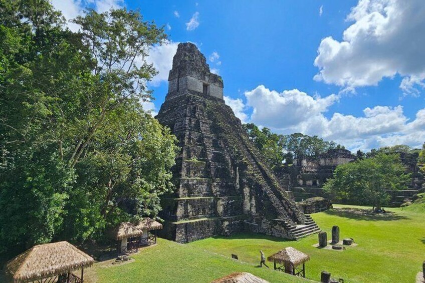 A Mayan pyramid surrounded by lush greenery and thatched-roof structures. 2