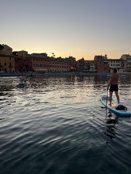 A person paddleboarding on calm water with buildings in the background. 1