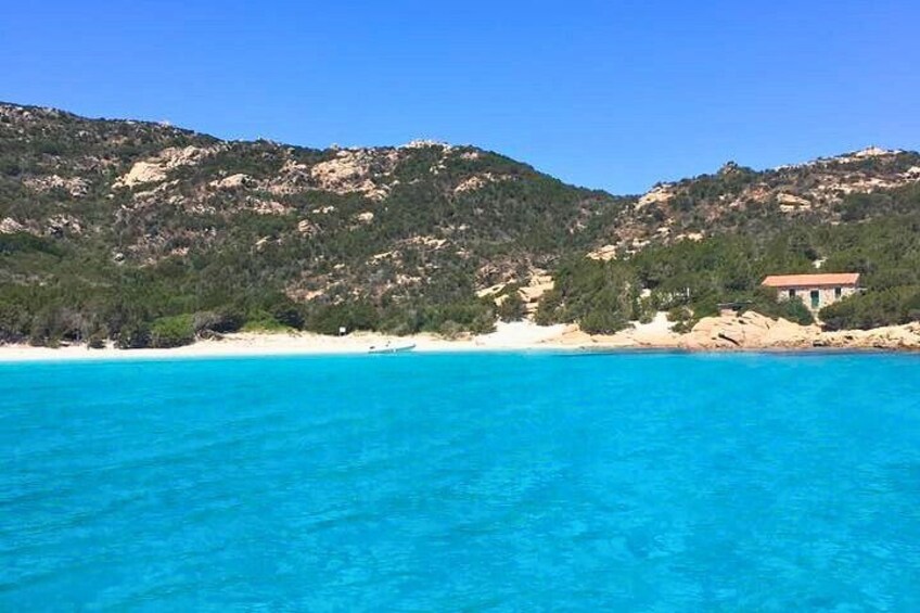 A coastal landscape with clear turquoise waters, a sandy beach, and a building on a hill. 5