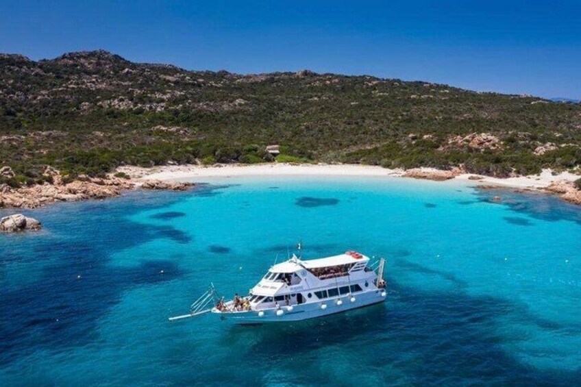 A boat on clear turquoise waters with a beach and rocky hills in the background. 1
