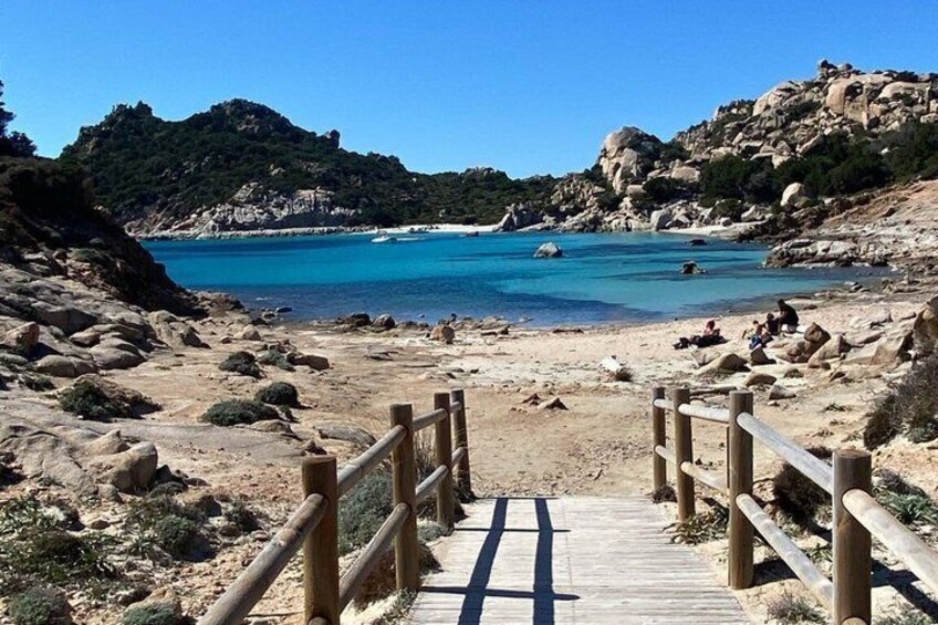 A beach with a wooden walkway leading to the water, surrounded by rocks and hills. 3