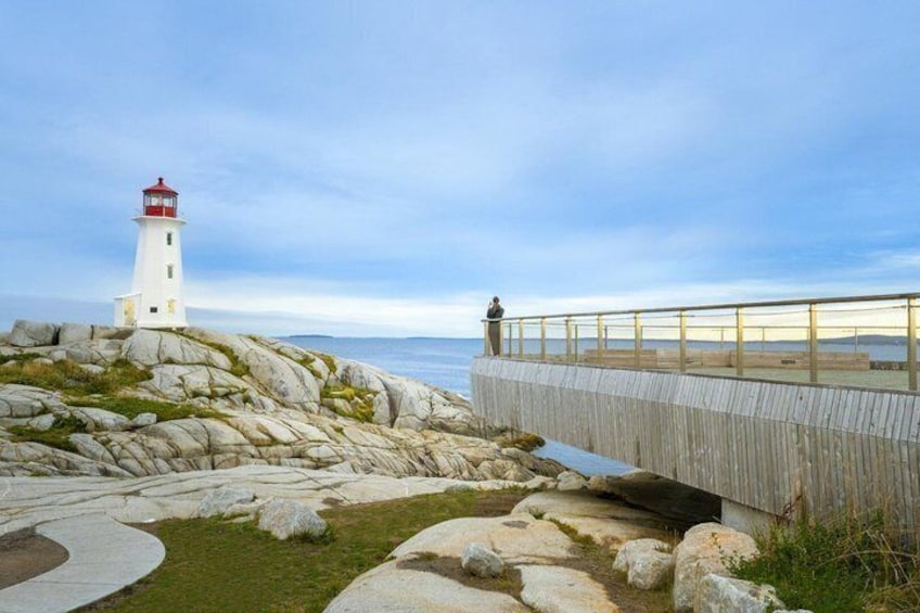 A lighthouse, rocky terrain, a wooden bridge, and a person standing on the bridge. 1