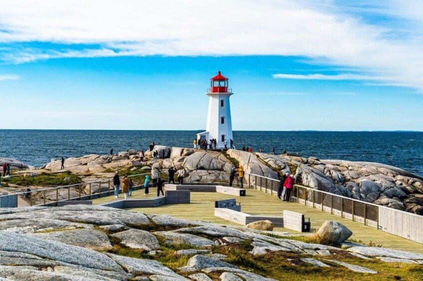 A lighthouse on a rocky coastline with people walking on the promenade. 2