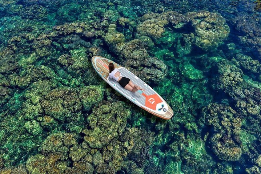 A person lying on a paddleboard in clear water with rocky underwater terrain. 3