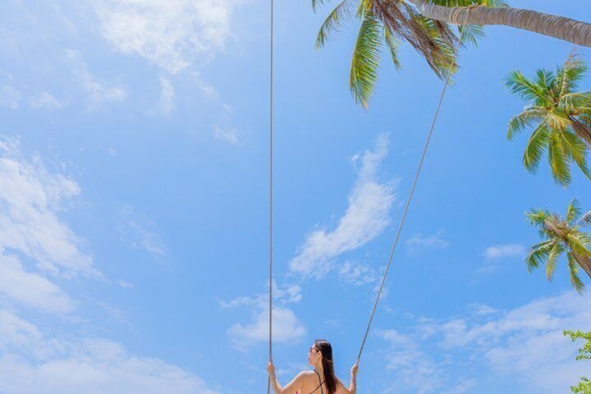 A person swinging on a rope between palm trees against a clear sky. 4