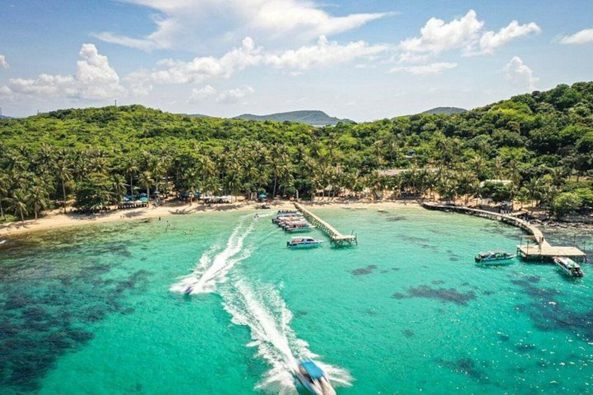 A tropical beach with clear turquoise waters, a pier, and lush green hills in the background. 1