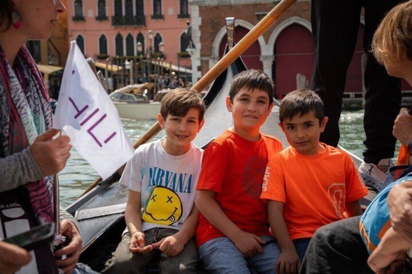 A gondola with passengers, including children, on a canal with historic buildings in the background. 2