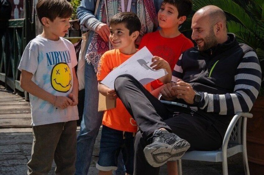 A man sitting on a chair with children around him, one holding a piece of paper. 4