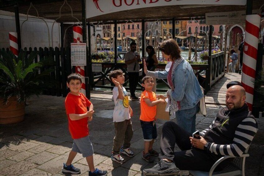 A group of people, including children, in an outdoor setting with a fountain and buildings in the background. 3