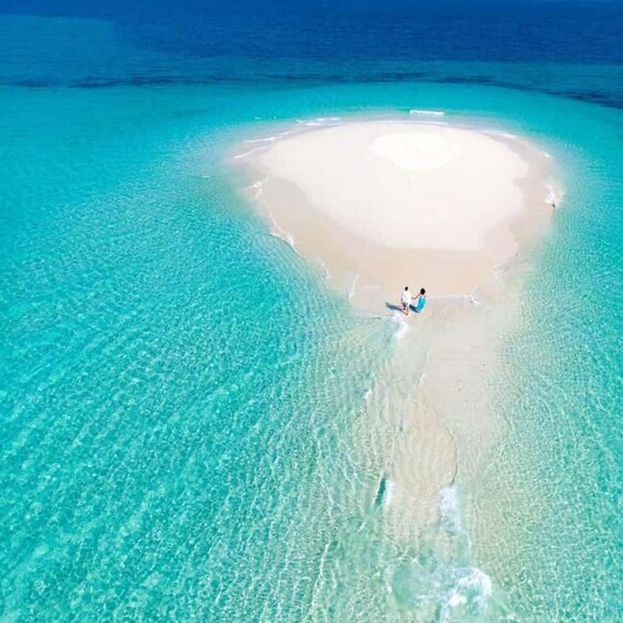 An aerial view of a turquoise lagoon with a white sandy beach and a person walking along the shore. 1