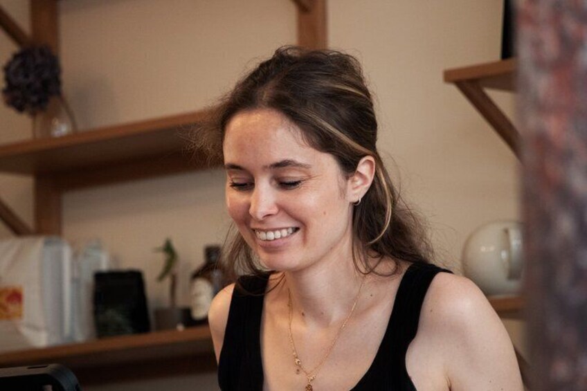 A person in a black tank top with a necklace, in a room with wooden shelves and various items. 4