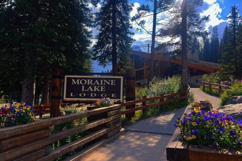 A wooden sign for Moraine Lake Lodge surrounded by a wooden fence and flower beds. 2