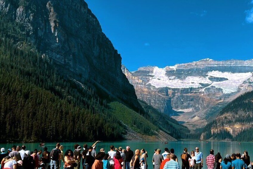 A group of people gathered by a lake with mountains in the background. 4