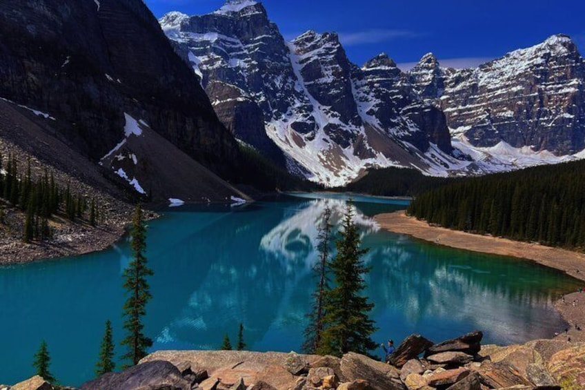 A mountain lake with clear turquoise water, surrounded by snow-capped peaks and dense forest. 1