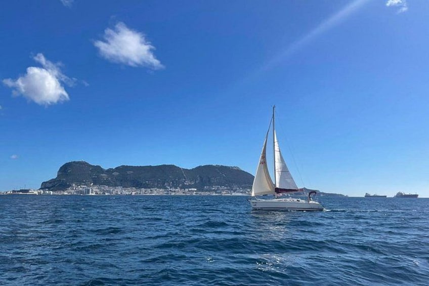 A sailboat on calm waters with a coastal cityscape in the background. 1