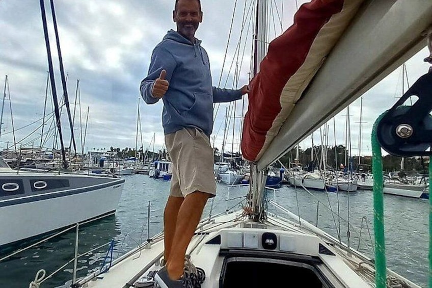 A person standing on a sailboat with a marina in the background. 2