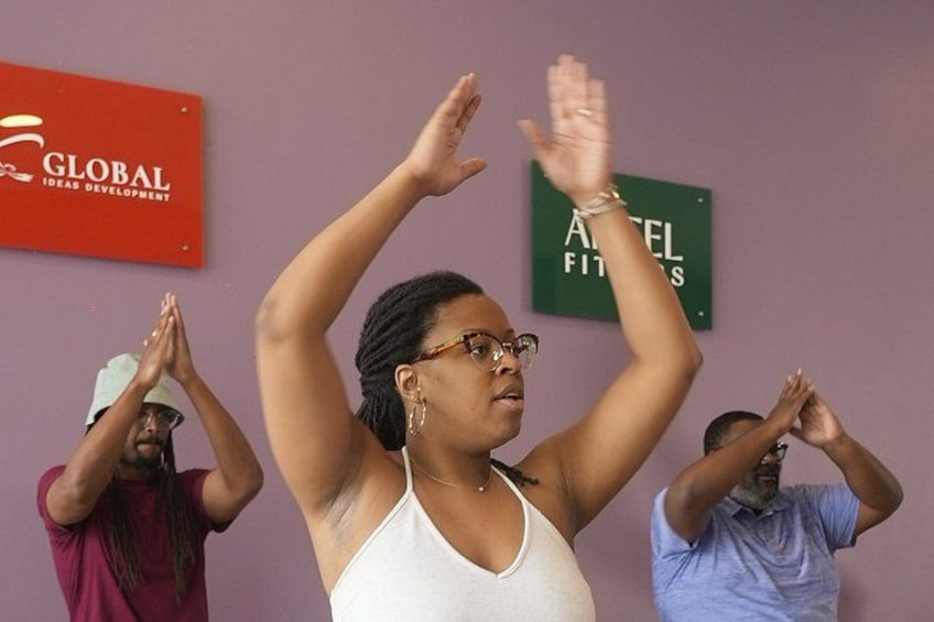 A person in a white tank top raising their arms, with two others in the background. 4