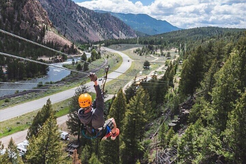 A person zip-lining over a mountainous landscape with a river and forested areas below. 4