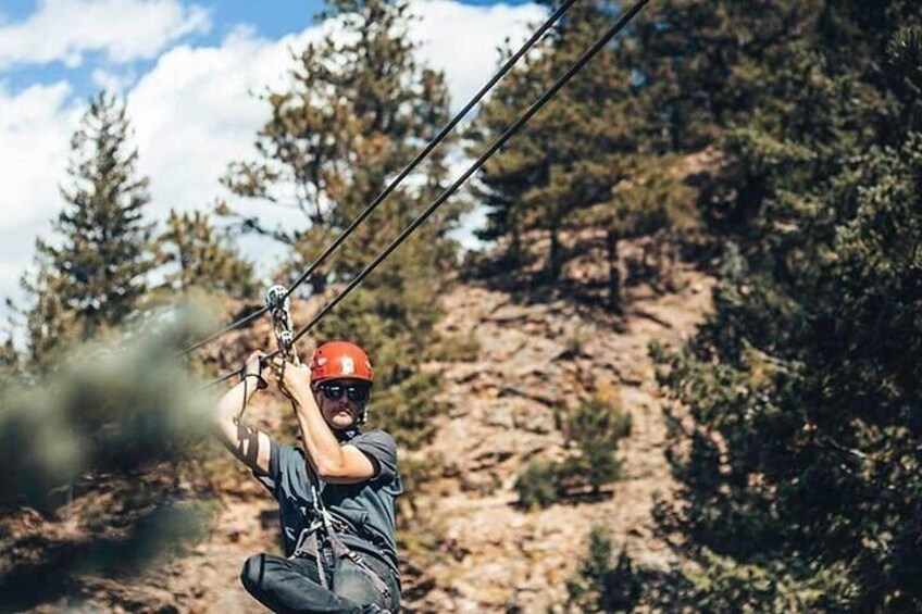 A person zip-lining through a forested area with trees and rocky terrain in the background. 5
