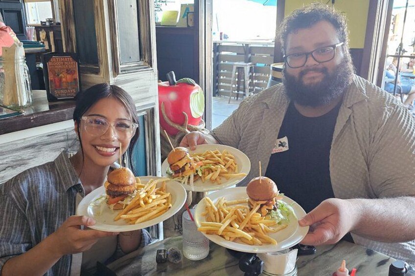 Two people holding plates of burgers and fries at a restaurant. 3
