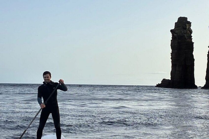 A person paddleboarding on calm waters with a large rock formation in the background. 5